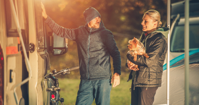 A couple holding a dog next to a caravan